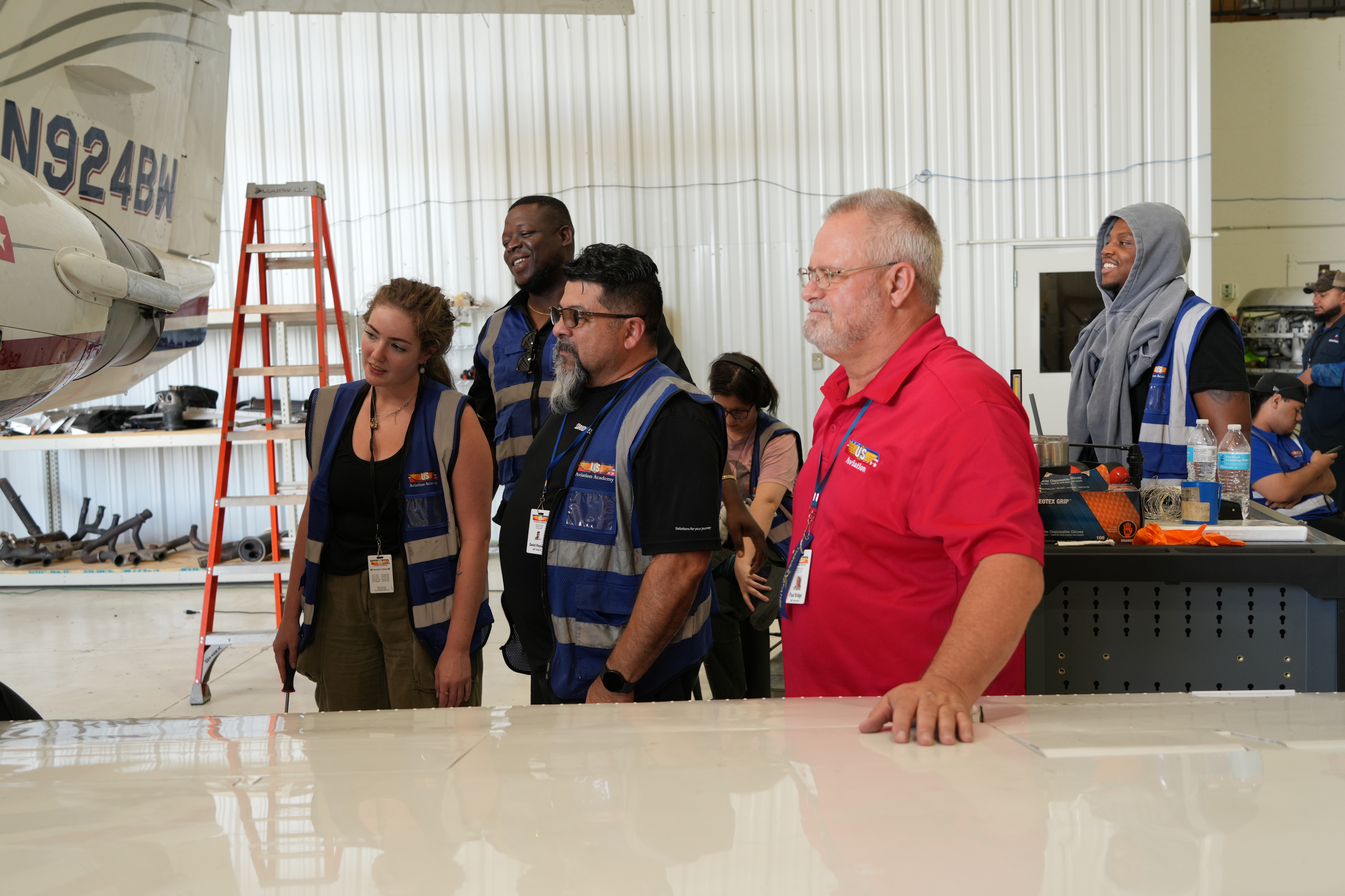 A group of aviation maintenance students and an instructor observing a demonstration inside an aircraft hangar.