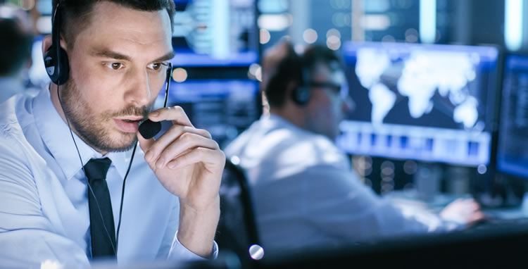 Air traffic controller wearing a headset speaking into a microphone while monitoring flight data on multiple screens.