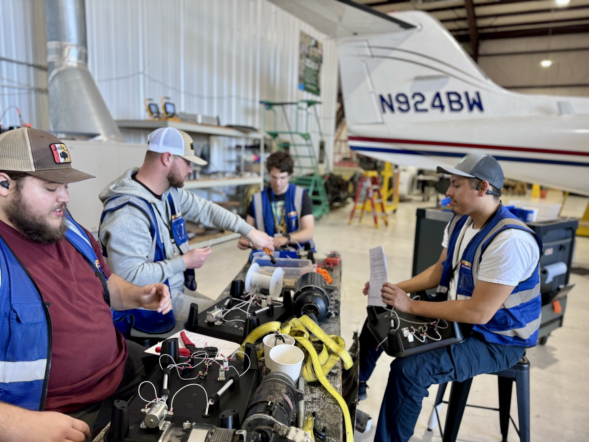 Group of aviation maintenance students working on hands-on electrical and avionics component training modules inside an aircraft hangar