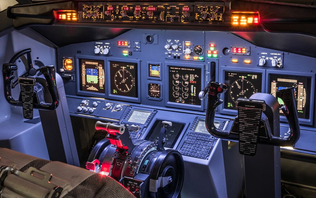 Commercial aircraft cockpit with illuminated control panels, flight instruments, and dual yokes.